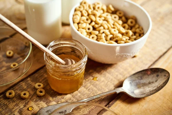 Café da manhã saudável tigela cheia de flocos de mel com mel dipper e leite na mesa de madeira — Fotografia de Stock