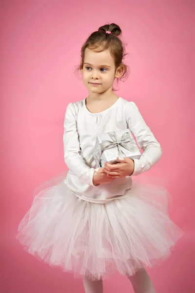 Menina bonito na saia de tule está segurando um presente em um fundo rosa — Fotografia de Stock
