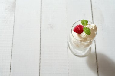 Tatlı taze nane yaprağı ve ahududu Beyaz ahşap masa üzerinde krem şanti ile bardak.