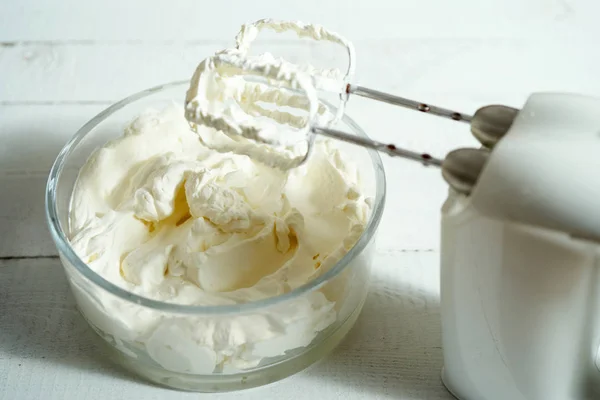 Parlak ahşap masanın üzerine bir kase ve elektrikli el mikseri krem şanti.