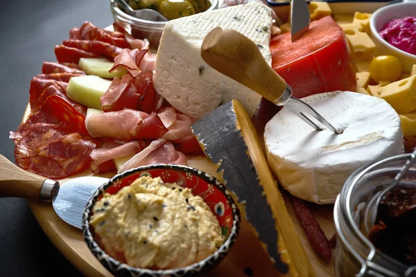Антипасті дошка з різними сиром і м'ясними закусками з гумусом і оливками на дерев'яній круглої дошці — стокове фото