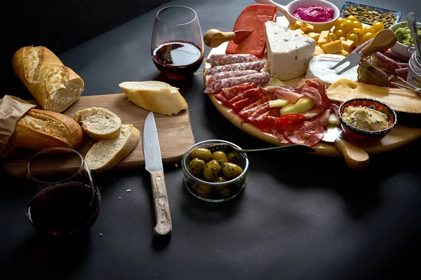 Placa antipasti com queijo e lanches de carne com vinho tinto e baguete a bordo na mesa preta — Fotografia de Stock