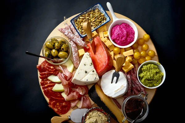 Placa antipasti com vários queijos e lanches de carne com húmus e azeitonas em tábua de madeira — Fotografia de Stock