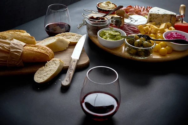 Antipasti board with cheese and meat snacks with red wine and baguette on board on black table — Stock Photo, Image