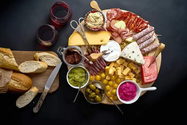 Антипасти с сыром и мясом закуски с красным вином и багет на борту на черном столе — стоковое фото