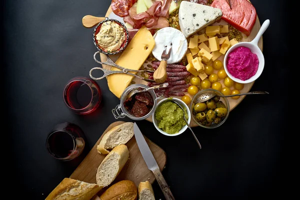 Tablero antipasti con aperitivos de queso y carne con vino tinto y baguette a bordo sobre mesa negra — Foto de Stock