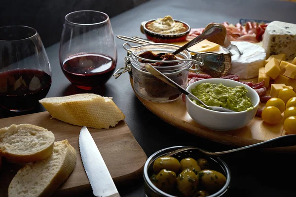 Placa antipasti com queijo e lanches de carne com vinho tinto e baguete a bordo na mesa preta — Fotografia de Stock