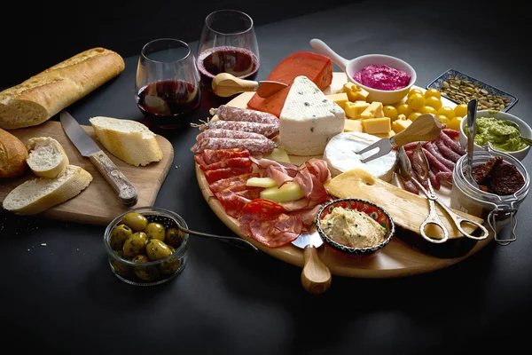 Placa antipasti com queijo e lanches de carne com vinho tinto e baguete a bordo na mesa preta — Fotografia de Stock