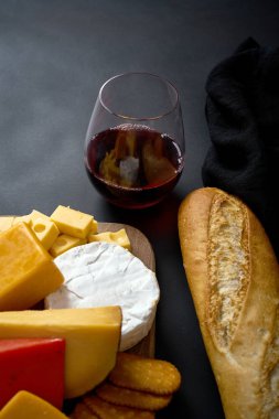Peynir ve baget çeşitli türleri ve siyah masada kırmızı şarap ile ahşap tahta