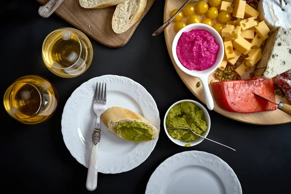 Антипасти с сыром и мясом закуски с белым вином и багет на борту на черном столе — стоковое фото