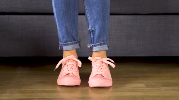 Mujer está sentada en un sofá gris y muestra sus piernas en cómodas zapatillas de coral o — Vídeo de stock