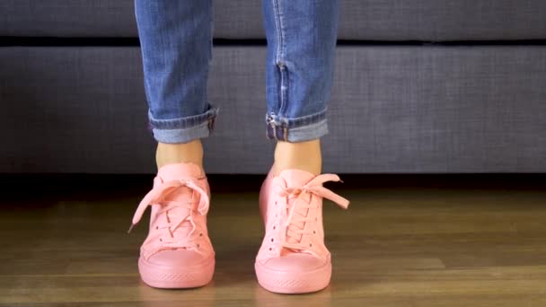 Woman standing by the sofa and showing her legs in comfortable coral sneakers — Stock Video