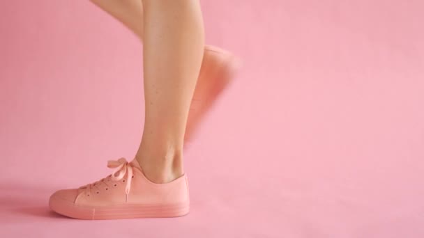 Acercamiento de piernas bien formadas femeninas caminando en zapatillas de deporte sobre fondo de coral — Vídeo de stock