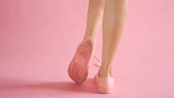Крупный план стройных женских ног, ходящих в кроссовках на коралловом фоне — стоковое видео