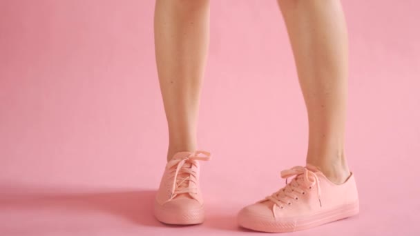 Close up of shapely female legs walking in sneakers on coral background — Stock Video