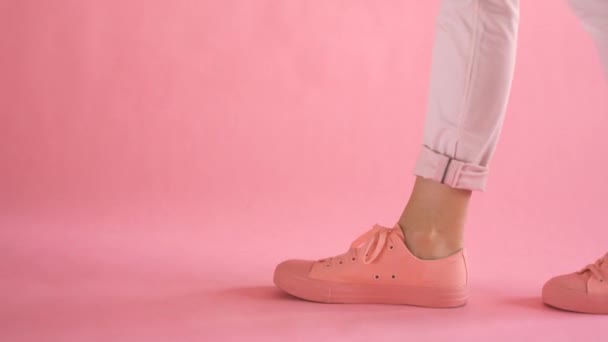 Acercamiento de piernas femeninas bien formadas caminando en zapatillas de deporte sobre fondo de coral — Vídeos de Stock