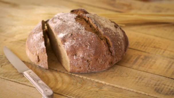 Dark homemade bread with sunflower seeds and wooden knife and ears of rye on wooden table — Stock Video