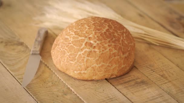 Złoty domowy chleb kukurydziany i drewniany nóż i uszy żyta na drewnianym stole — Wideo stockowe