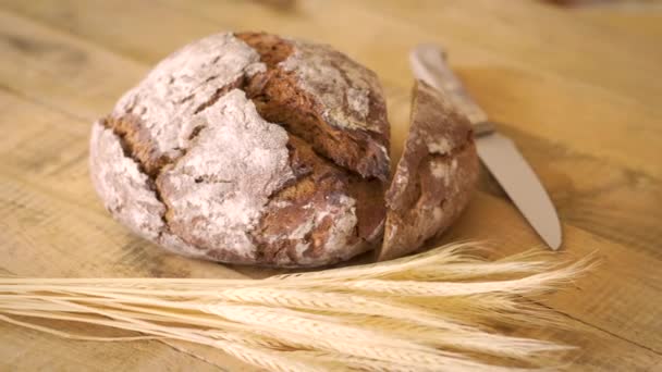 Donker zelfgebakken brood met zonnebloempitten en houten mes en oren van rogge op houten tafel — Stockvideo