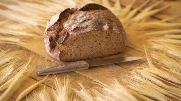 Тёмный домашний хлеб с семенами подсолнечника, деревянным ножом и ржаными ушами на деревянном столе — стоковое видео