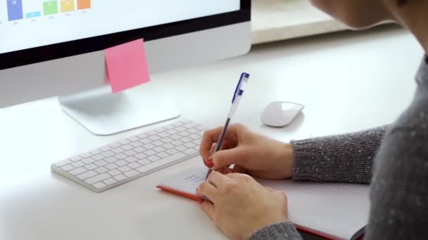 女性双手在电脑键盘旁边的笔记本上写字 — 图库视频影像