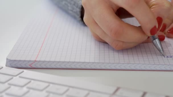 Gros plan des mains féminines écrire une note dans le carnet à côté du clavier d'ordinateur blanc 