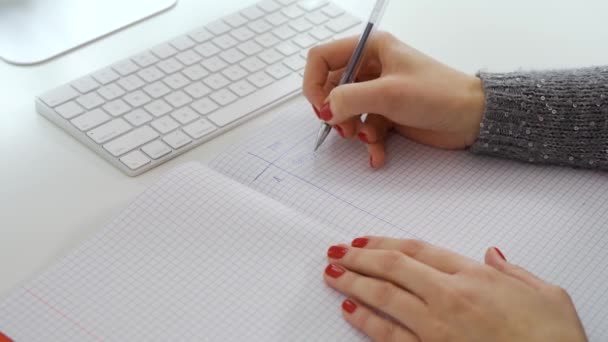 Weibliche Hände schreiben Notizen in Notizbuch neben weißer Computertastatur — Stockvideo