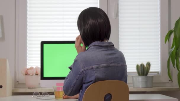 Vue arrière de la femme travaillant sur le clavier de l'ordinateur et parlant sur le téléphone devant l'écran vert isolé — Video