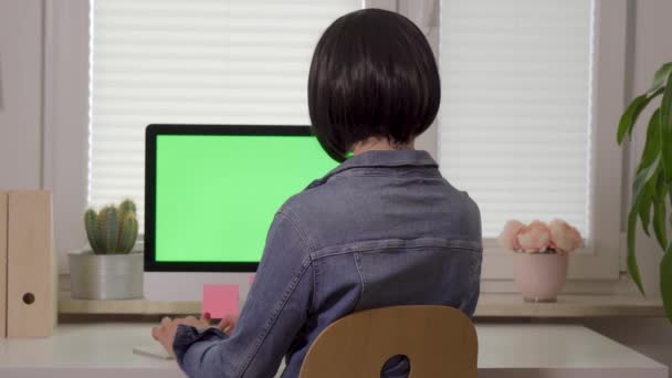 Vista posterior de la joven mujer que trabaja en el teclado de la computadora en frente de la pantalla con pantalla verde aislada — Vídeo de stock