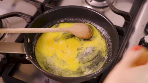 Mujer prepara y mezcla huevos revueltos en la cacerola en la estufa de gas en la cocina casera — Vídeos de Stock