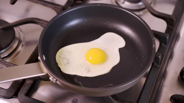 Woman in home kitchen frying fried egg in pan for breakfast on gas stove — Stock Video