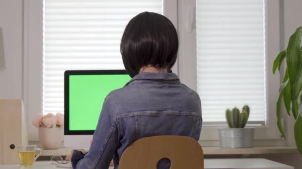 Rückansicht einer an der Computertastatur arbeitenden Frau vor einem Bildschirm mit isoliertem grünem Bildschirm — Stockvideo