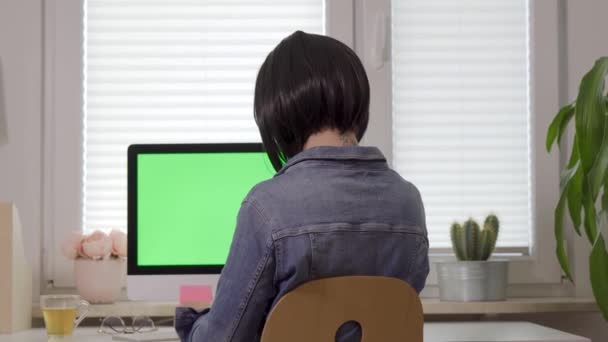 Back view of woman working on computer keyboard and talking on the phone in front of display with isolated green screen — Stock Video