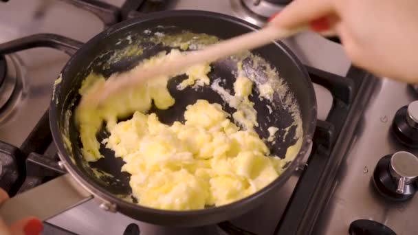 Γυναίκα ετοιμάζει και αναμιγνύει ανακατωμένα αυγά σε τηγάνι για το φυσικό αέριο σόμπα στην κουζίνα στο σπίτι — Αρχείο Βίντεο