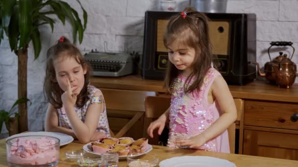 두 어린 소녀는 크림에 넣어 나무 테이블에 맛있는 컵 케이크를 장식 — 비디오