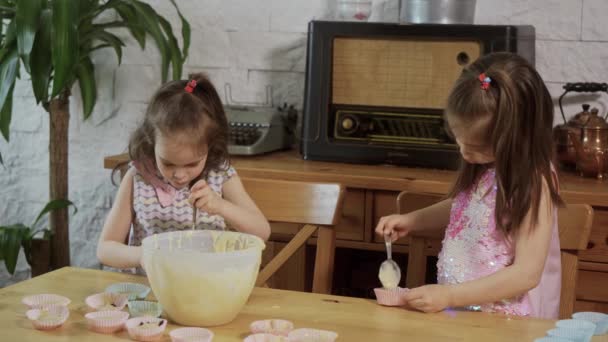 Twee kleine meisjes zetten crème op de mallen om cupcakes te maken — Stockvideo