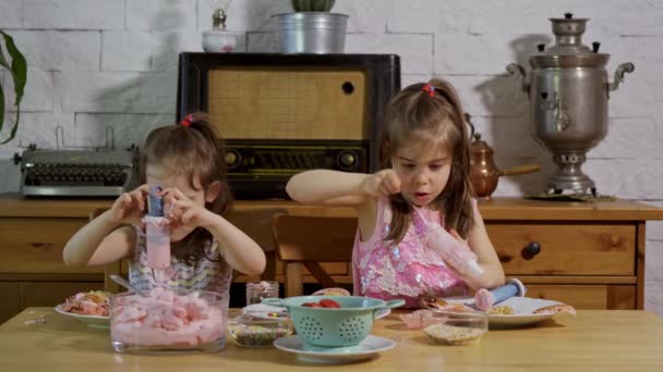 Två små flickor sätta på en kräm och dekorera läckra muffins på ett träbord — Stockvideo
