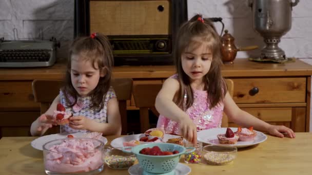 Due bambine si mettono una crema e decorano deliziosi cupcake su un tavolo di legno — Video Stock