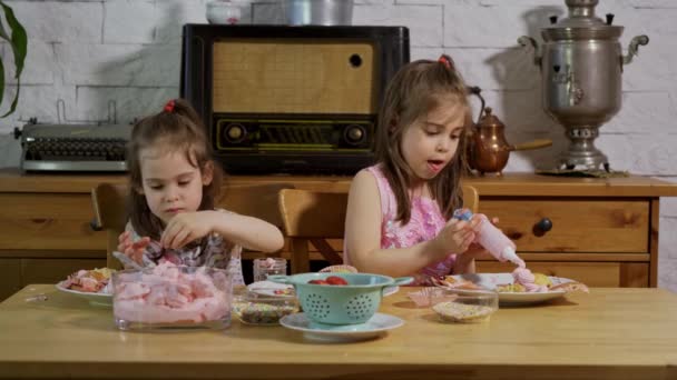 Två små flickor sätta på en kräm och dekorera läckra muffins på ett träbord — Stockvideo