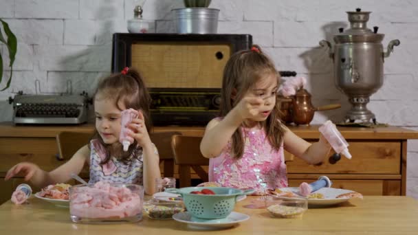 Two little girls put on a cream and decorate delicious cupcakes on a wooden table — Stock Video