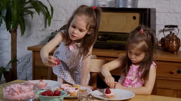 二人の小さな女の子はクリームを置き、木製のテーブルの上においしいカップケーキを飾ります — ストック動画