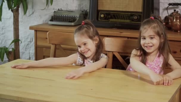 Twee kleine meisjes lachen en praten op een houten tafel — Stockvideo