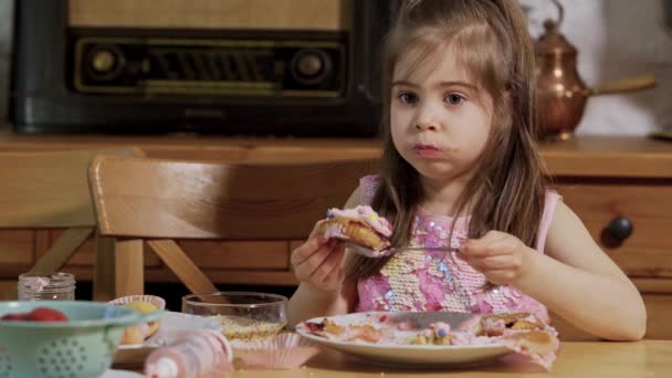 Kleines Mädchen schmückt und isst leckere Cupcakes — Stockvideo