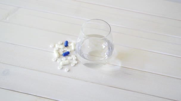 Szklanka Kryształowej wody i zestaw tabletek na białym drewnianym stole — Wideo stockowe