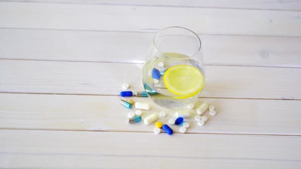 Verre d'eau cristalline avec citron et ensemble de pilules sur table en bois blanc — Video