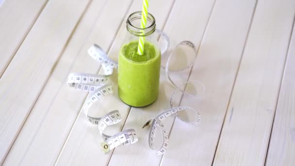 Здоровый зеленый и веганский коктейль с сантиметровой лентой на белом деревянном столе — стоковое видео