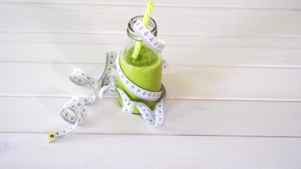 Здоровый зеленый и веганский коктейль с сантиметровой лентой на белом деревянном столе — стоковое видео