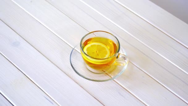 Скляна чашка з традиційним китайським чаєм і скибочкою лимона на білому столі . — стокове відео