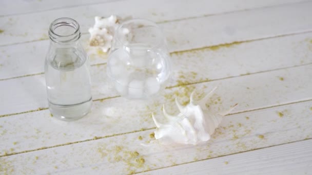 Verre avec eau et coquillages blancs sur table en bois avec sable — Video