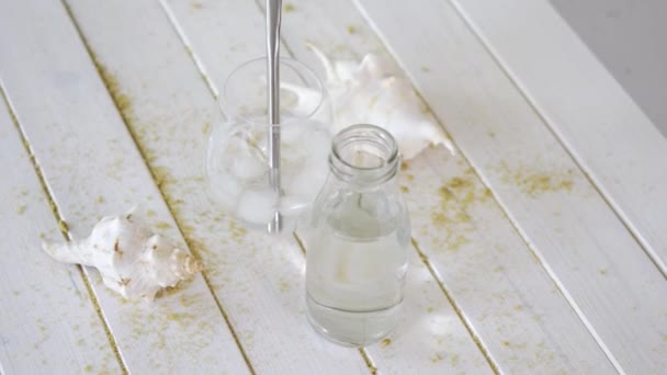 Bicchiere con acqua con paglia di titanio e conchiglie bianche su tavolo di legno con sabbia — Video Stock